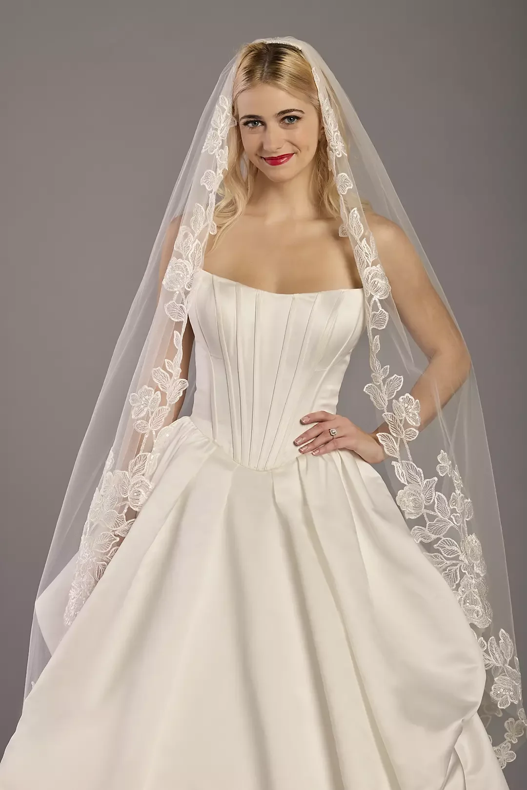 A woman wearing a wedding dress with a veil embroidered with floral patterns.