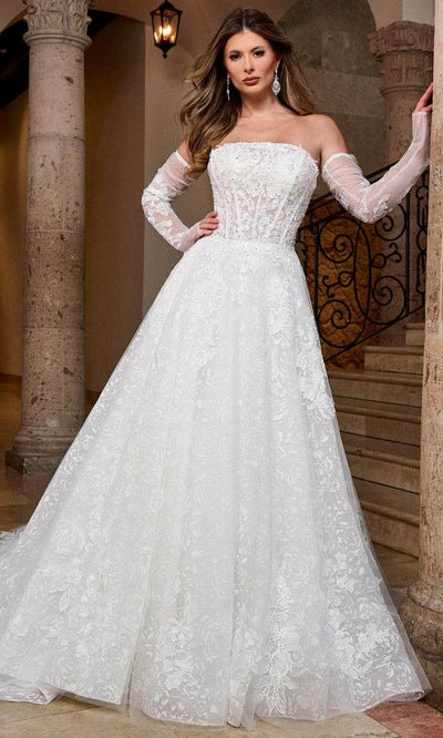 Woman in a white wedding dress with lace details, off-shoulder sleeves, standing inside a building with stone columns and staircase.
