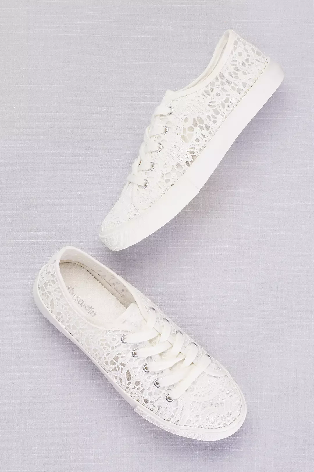 Two white lace sneakers with white laces on a light purple background.
