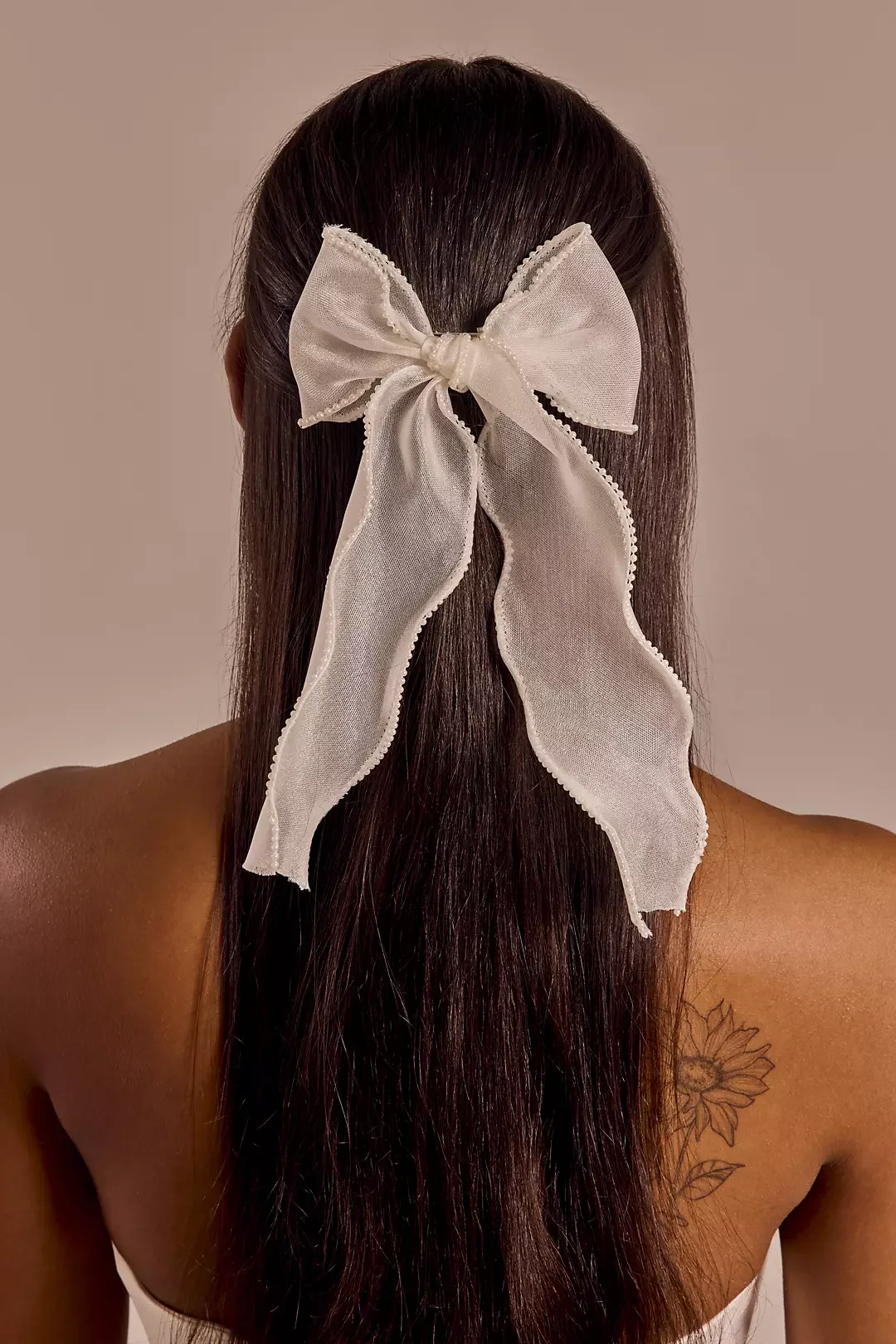 Back view of a woman with long, dark hair tied with a large, sheer, white bow.