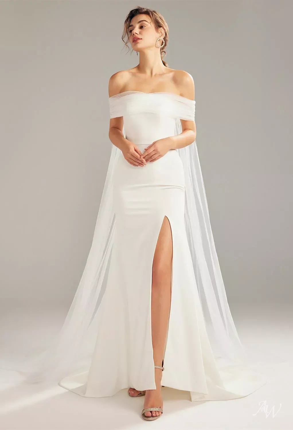 A woman wearing a white off-the-shoulder gown with a high slit, standing against a plain background.
