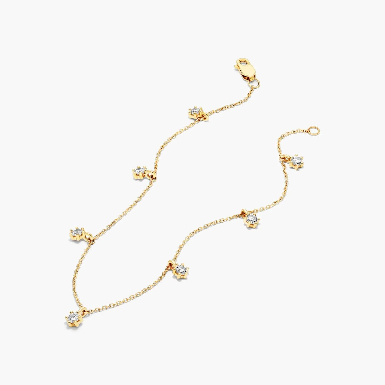 Gold necklace with small flower-shaped charms with clear stones, laid out on a white background.
