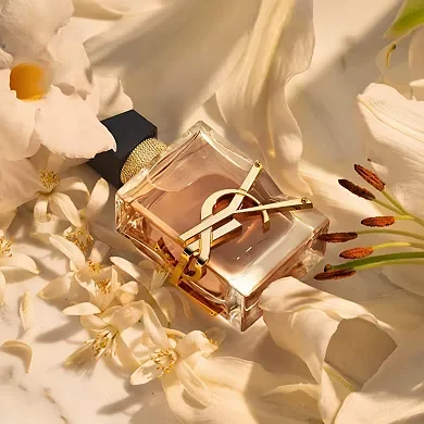 A bottle of Yves Saint Laurent Mon Paris perfume surrounded by white and cream flowers on a soft, satin fabric background. Empress archetypes Perfume vibes.