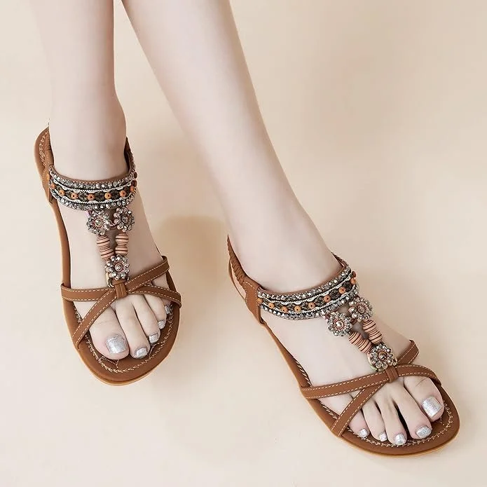 Person wearing brown sandals with decorative beads and jewels, showing painted toenails.