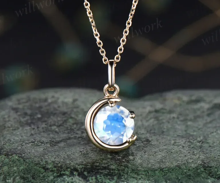 Silver necklace with a crescent moon pendant holding a large, clear gemstone, resting on a textured surface.