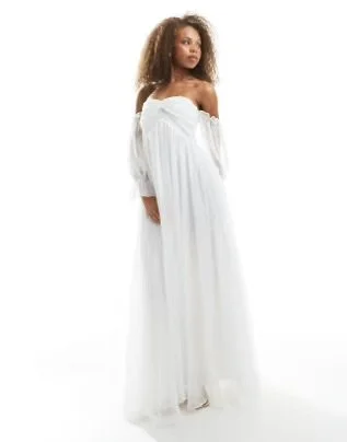 A woman with curly hair wearing an off-shoulder white dress.