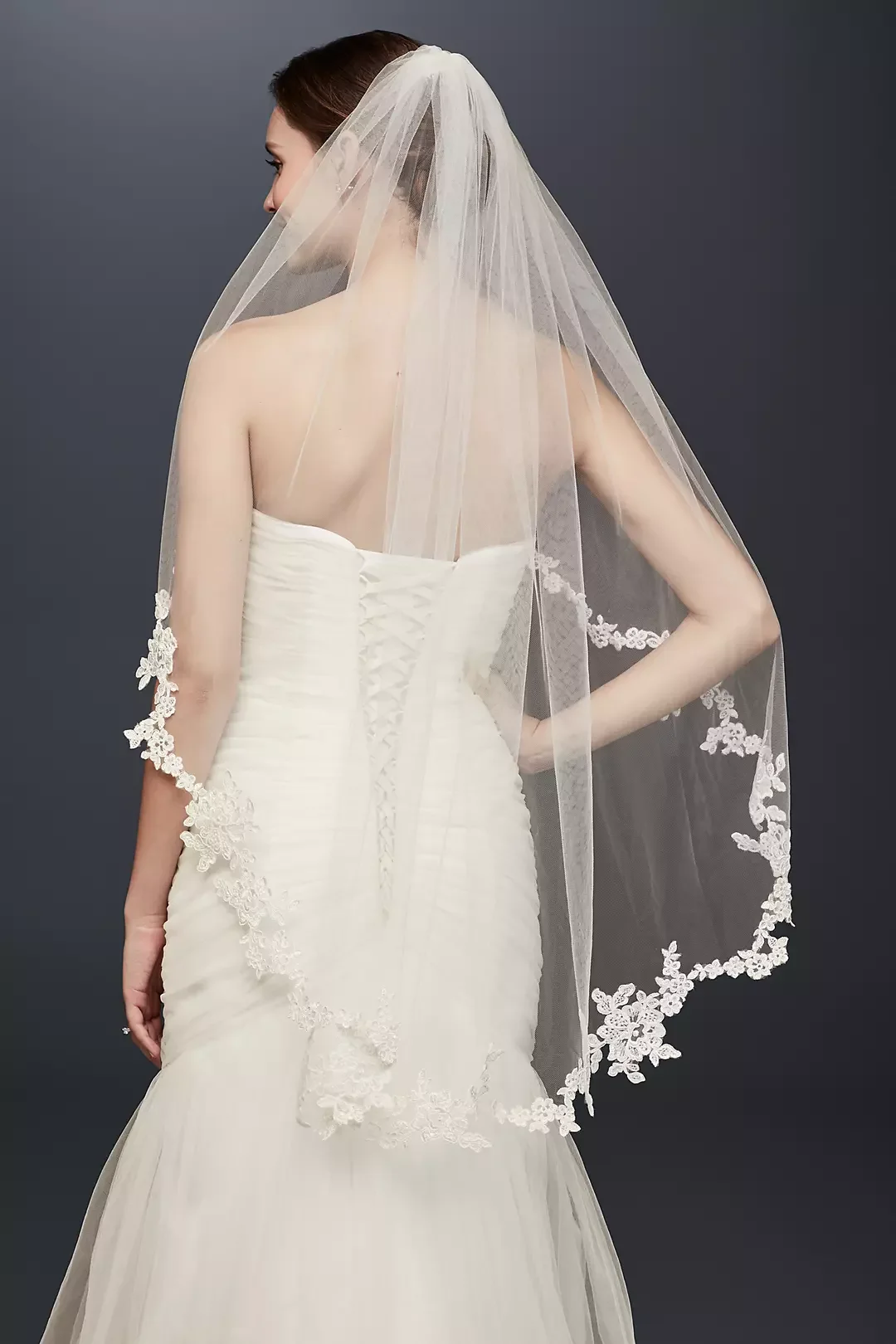 A woman in a strapless white wedding dress with lace details and a long veil with floral embroidery.