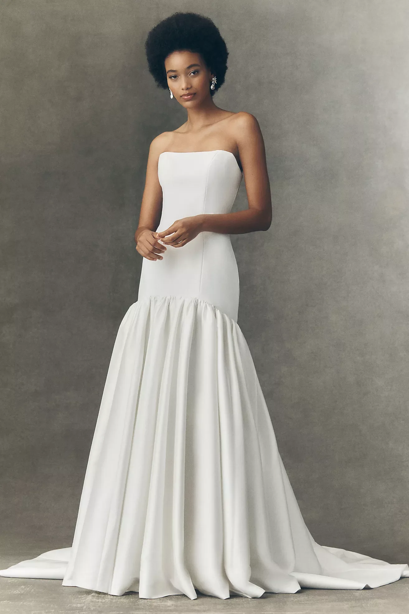 A woman in a strapless white gown with a ruffled bottom, standing against a neutral background.