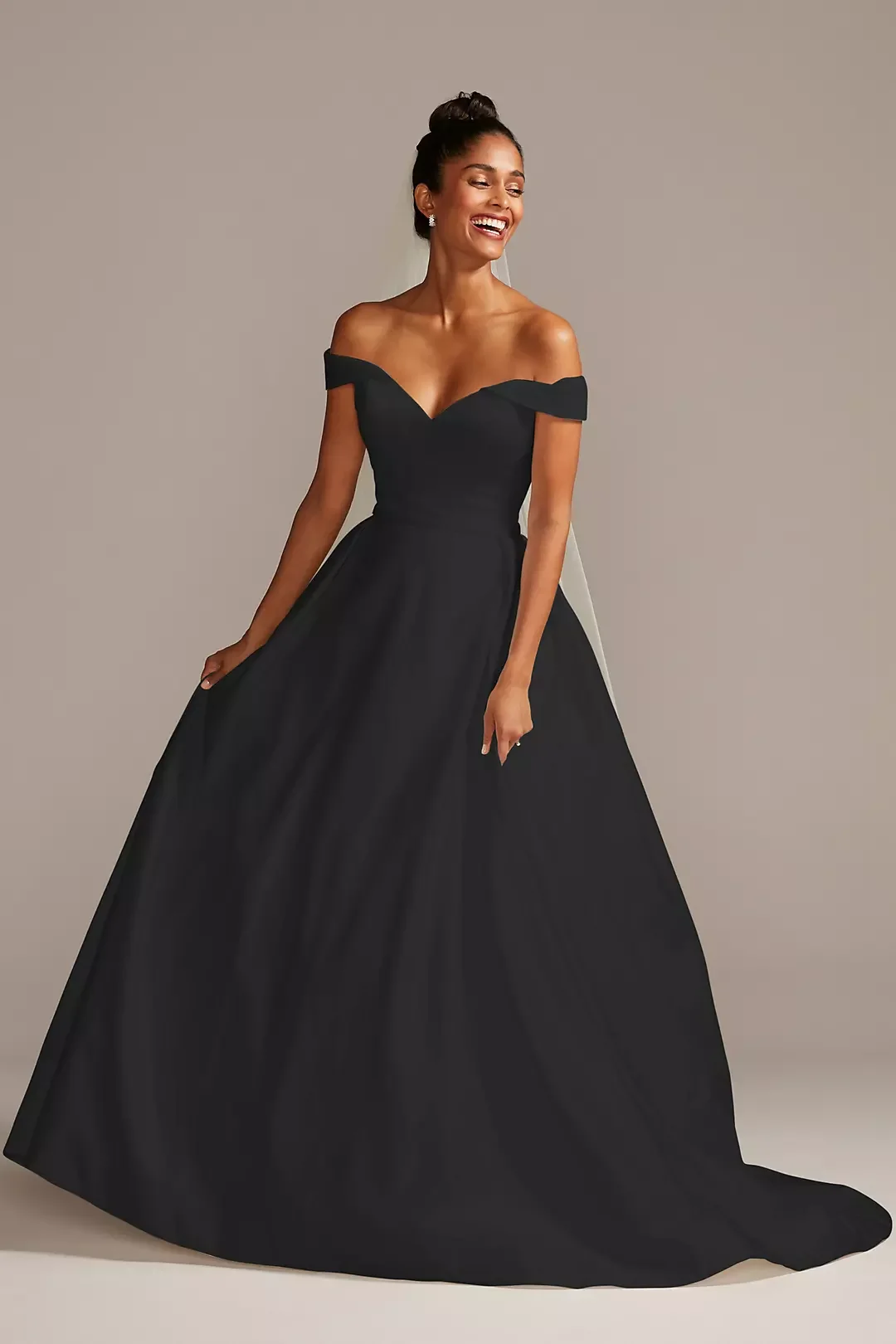 Woman in a strapless black ball gown, smiling and standing against a plain background.