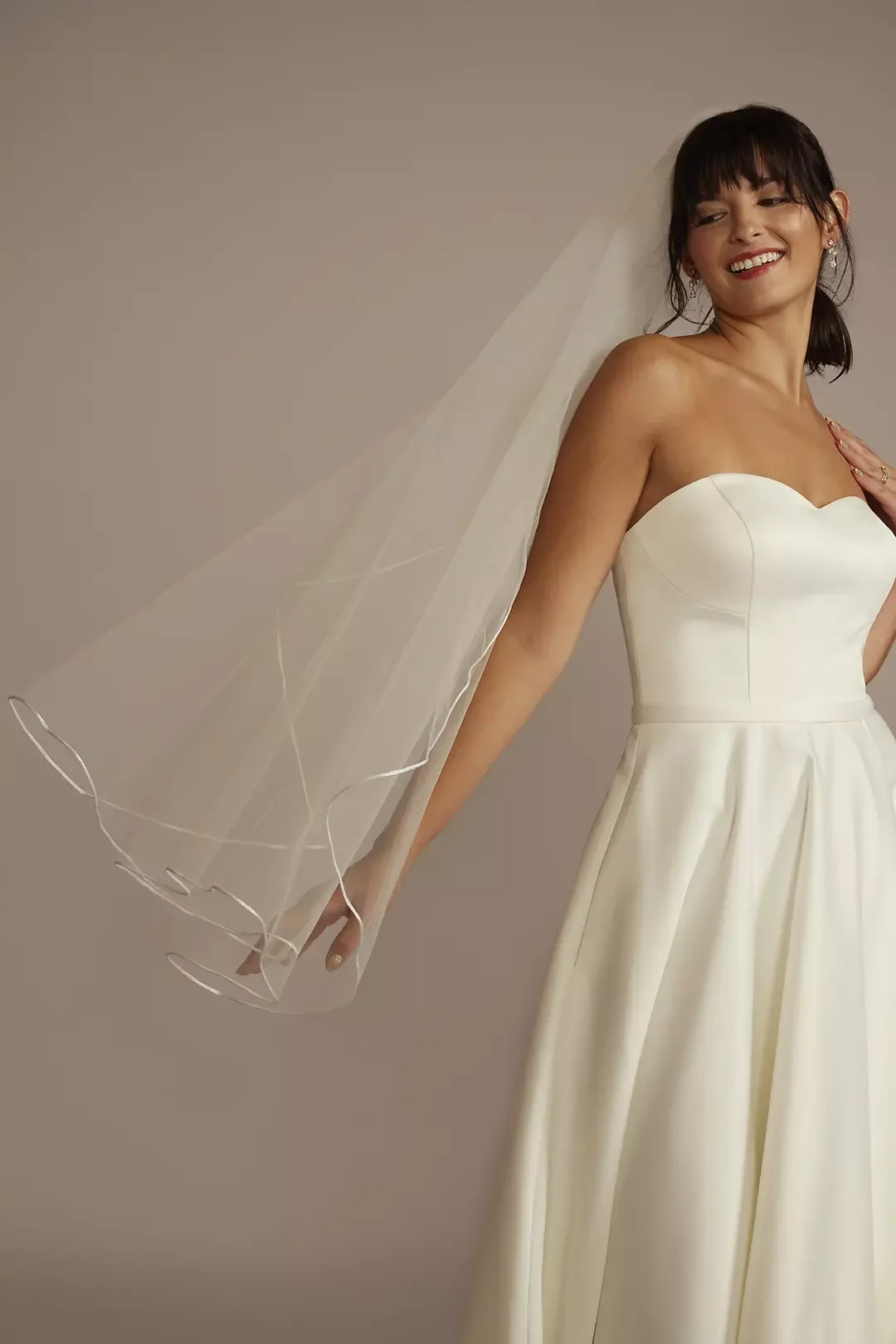 A woman in a strapless wedding dress with a veil, smiling and posing.
