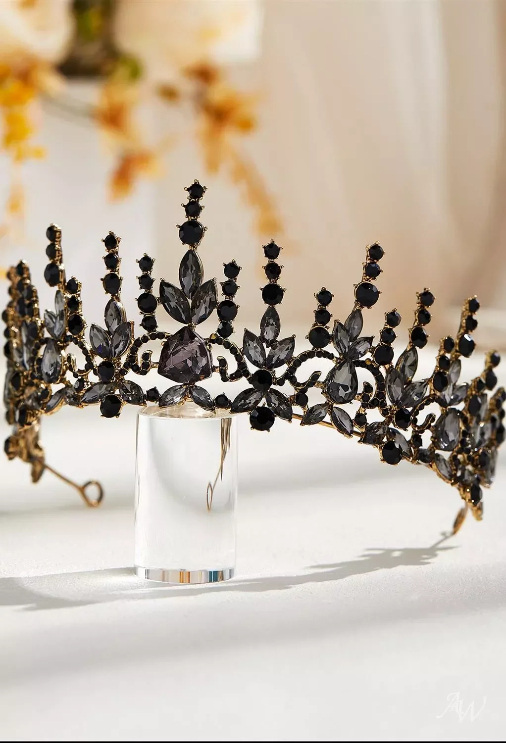 A black and gold tiara with black and clear gemstones resting on a clear stand