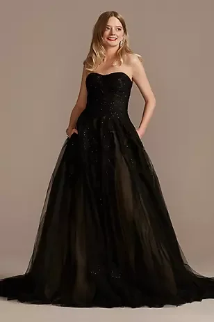 Woman wearing a strapless black gown with a full tulle skirt, standing and smiling.