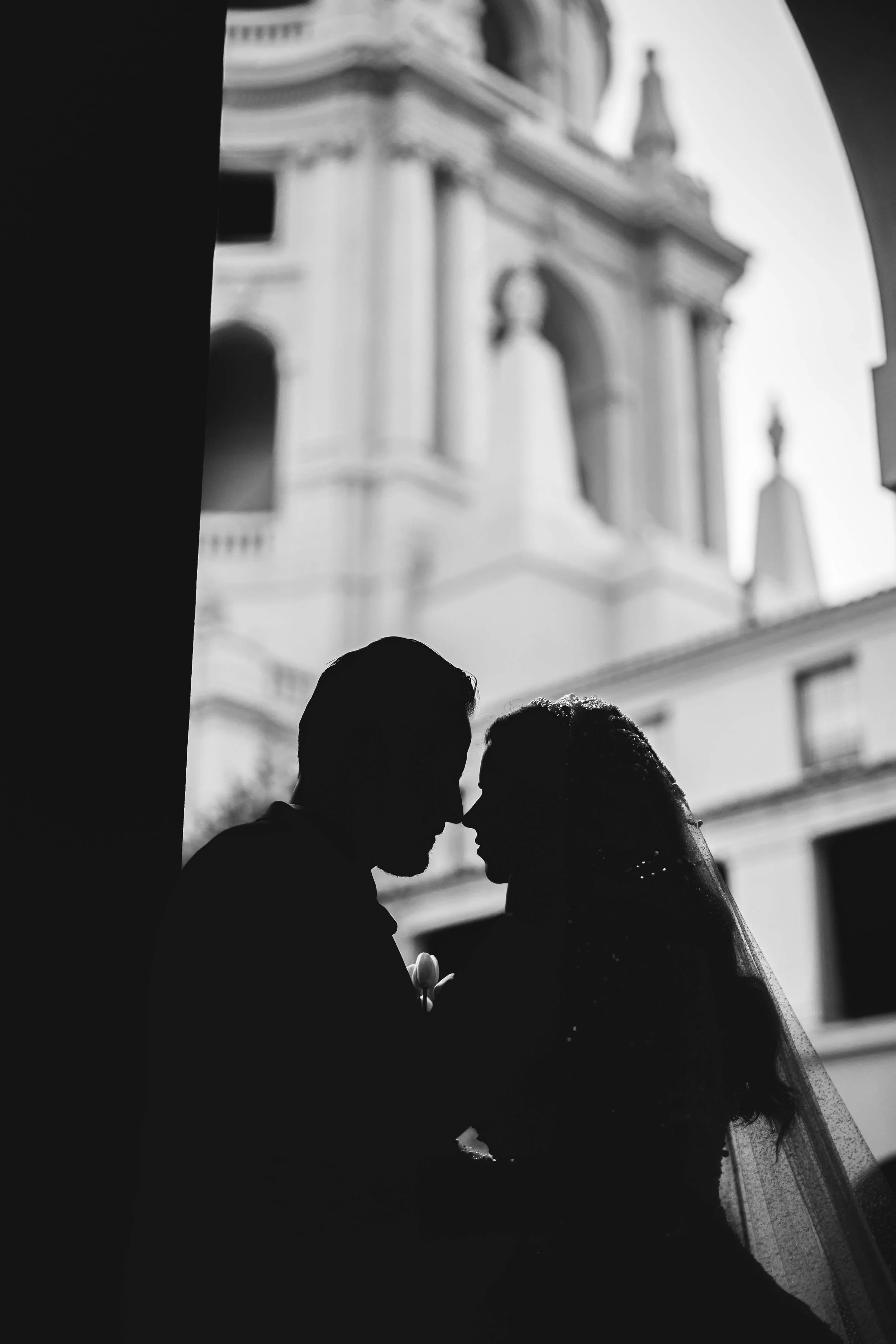 Silhouetted couple, possibly bride and groom, kissing outside a building with classical architecture, with a tower and statues in the background, Pasadena City Hall