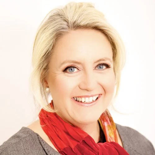 A smiling woman with blonde hair, wearing a gray top and a red scarf.