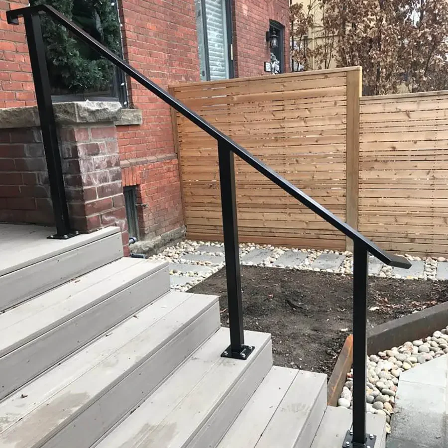 Exterior view of a house showing a staircase with wooden steps, a black metal handrail, brick exterior wall, and a wooden privacy fence.