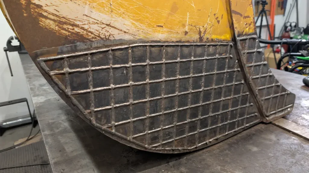 Close-up of a metal industrial part with a grid pattern, attached to a yellow surface, in a workshop.