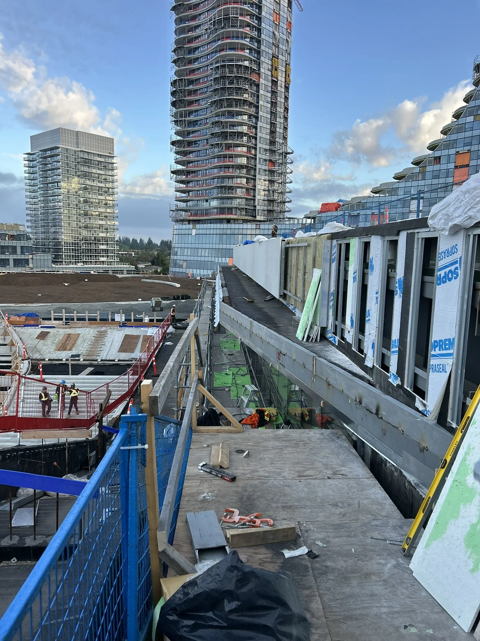 Construction work on a building with scaffolding, safety rails, and construction tools, set against a backdrop of modern high-rise buildings and a partly cloudy sky.