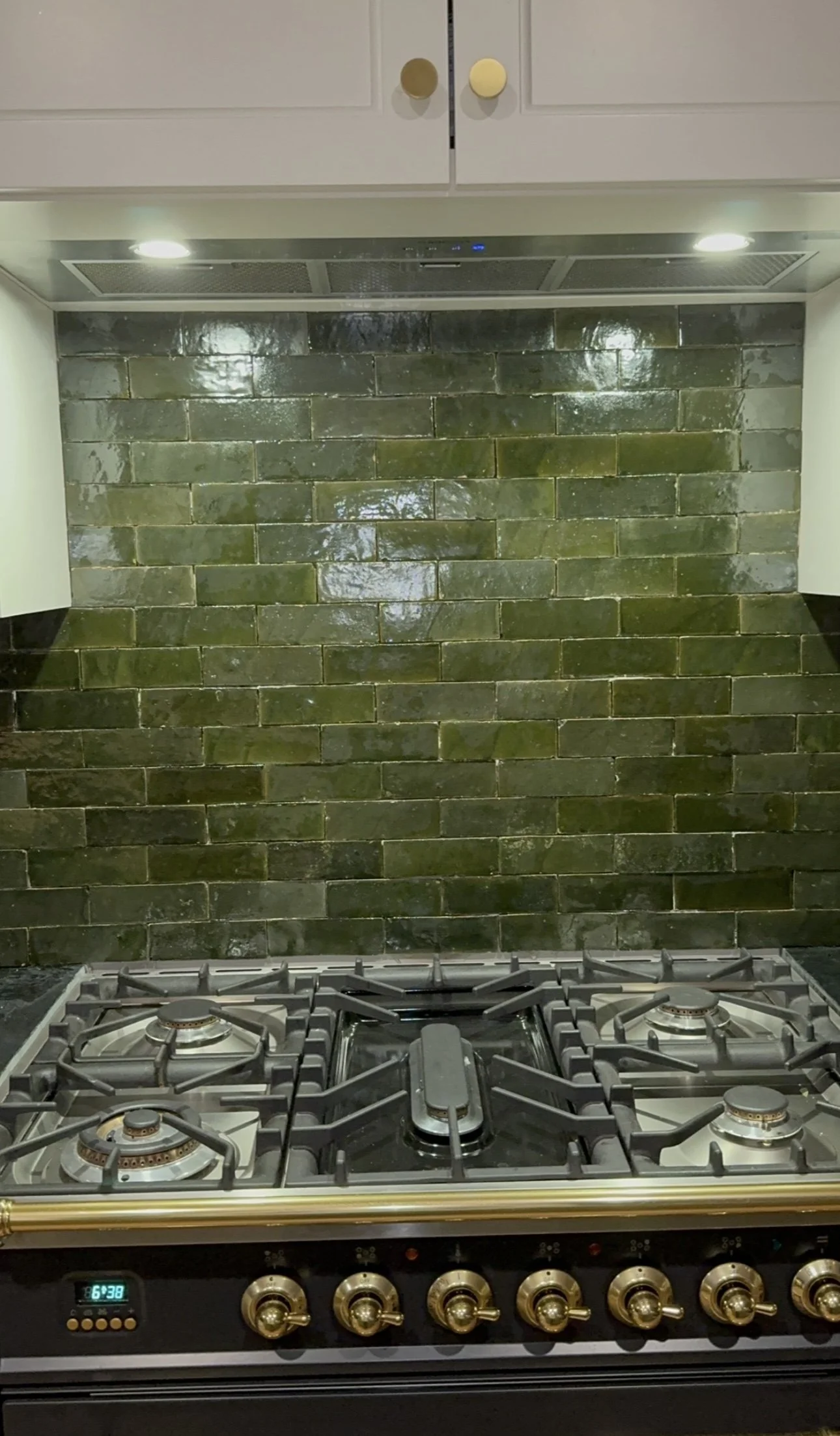 Green tile backsplash above a stainless steel gas stove in a kitchen.
