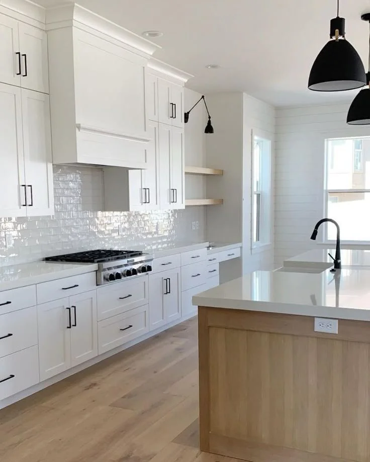 A modern kitchen with white cabinets, a white countertop, a black faucet, open shelving, and black pendant lights.