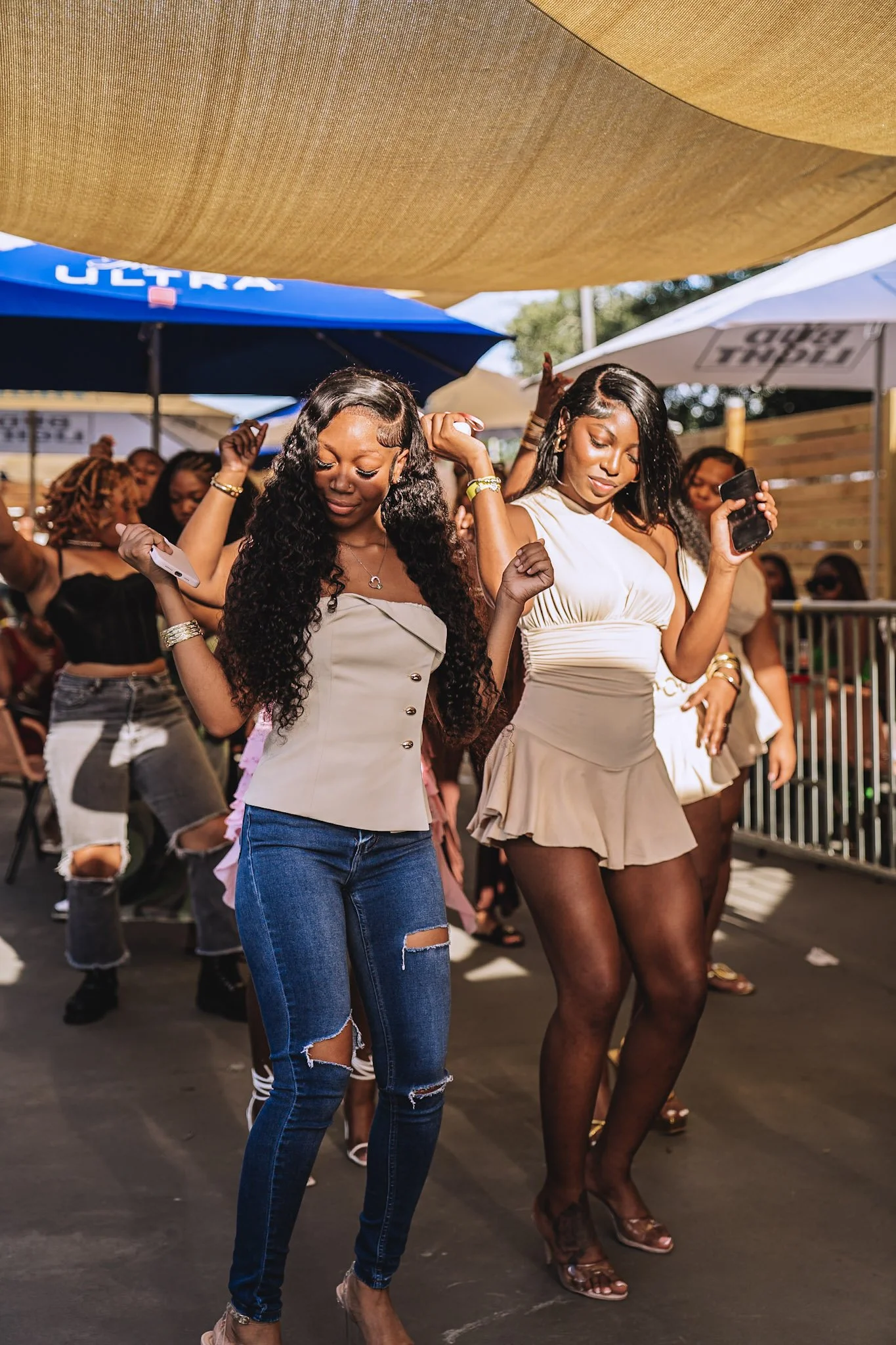 Two women dancing at an outdoor event under large umbrellas, with other people in the background.