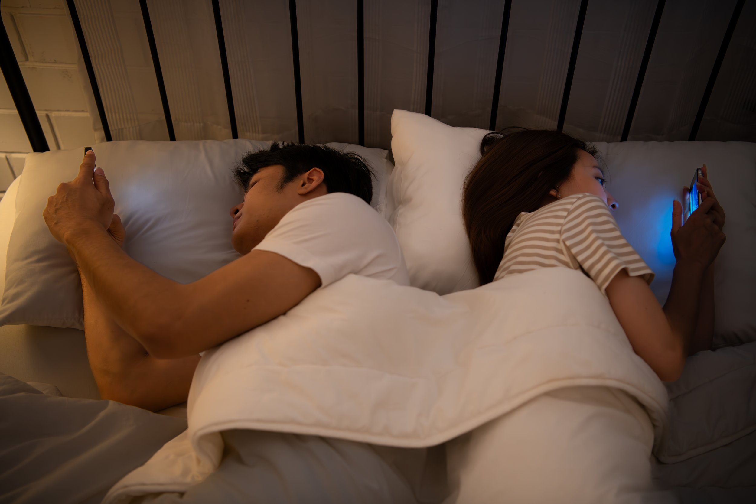 Couple in bed facing away from each other looking on their phones