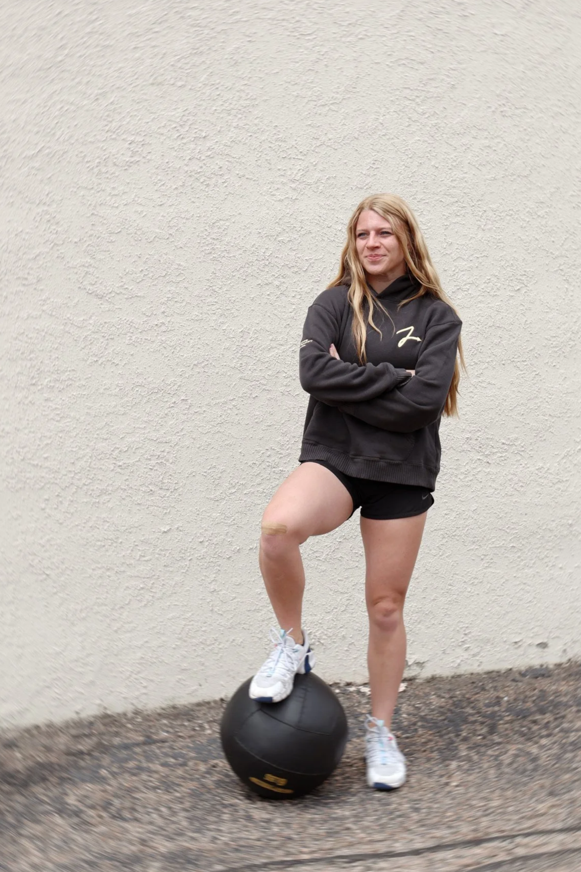 Coach Dakota standing with her foot propped up on a medicine ball in a Zenith Pro hoodie