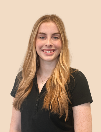 Young woman with long blonde hair wearing a black polo shirt, smiling against a beige background.