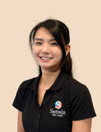 A young woman with long dark hair wearing a black polo shirt with the Sensia logo, smiling, against a beige background.