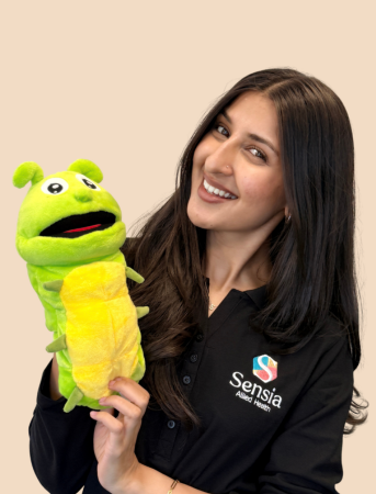 Woman in a black shirt holding a green frog puppet with a cheerful expression