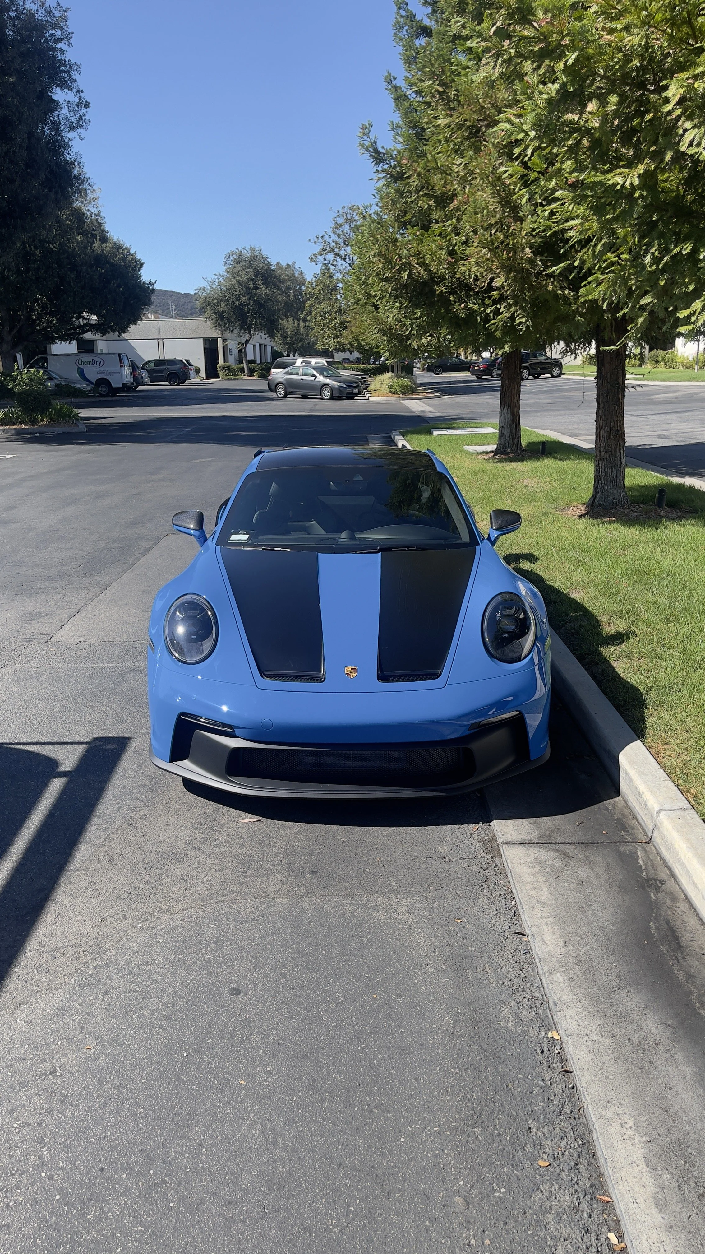 A blue Porsche 911 with a black racing stripe parked in a parking lot. A close-up view of a blue and black Porsche gt3 wrapped with custom satin black lettering vinyl wrap