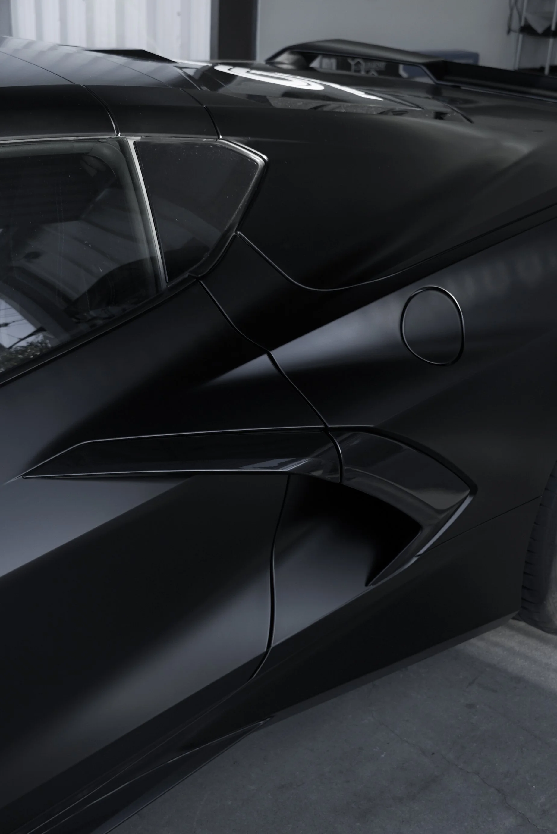 Close-up of a sleek black sports car with sharp lines and angular design features. Satin black colored paint protection film wrapped on corvette c8