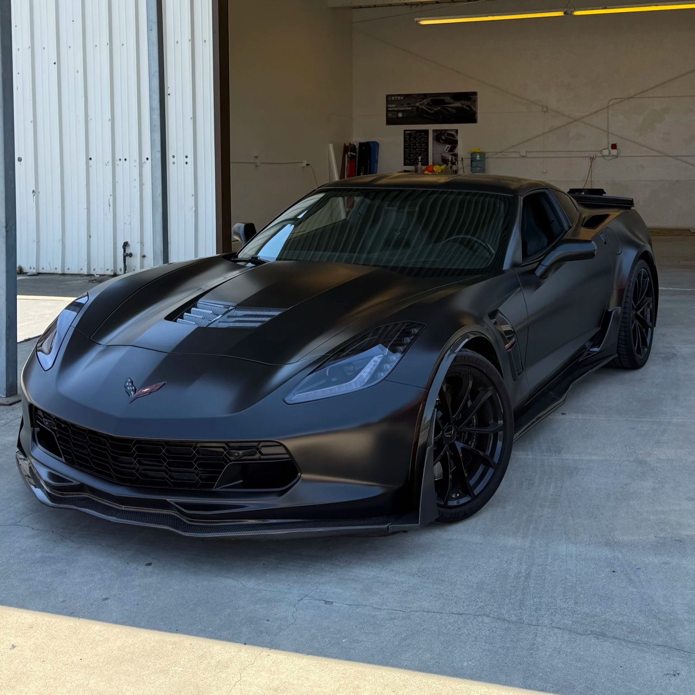 A black sports car with a sleek design inside a garage. corvette c7 wrapped in satin black vinyl wrap