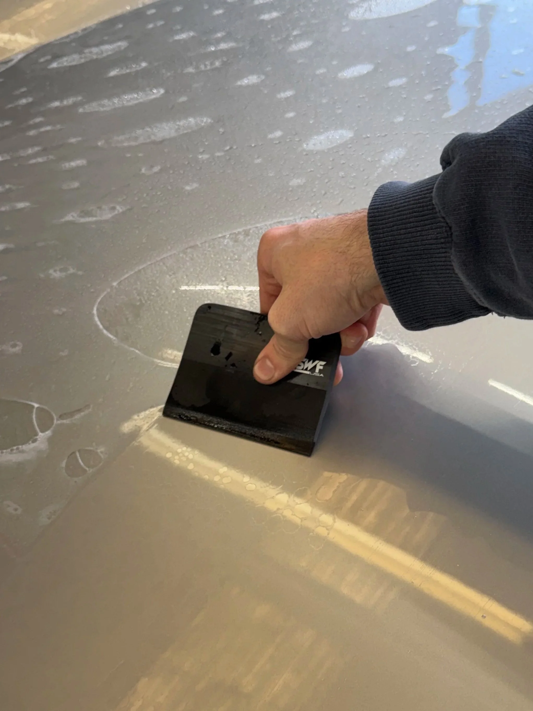 Person using a squeegee to apply PPF (Paint Protection Film) on a Porsche cayman S hood