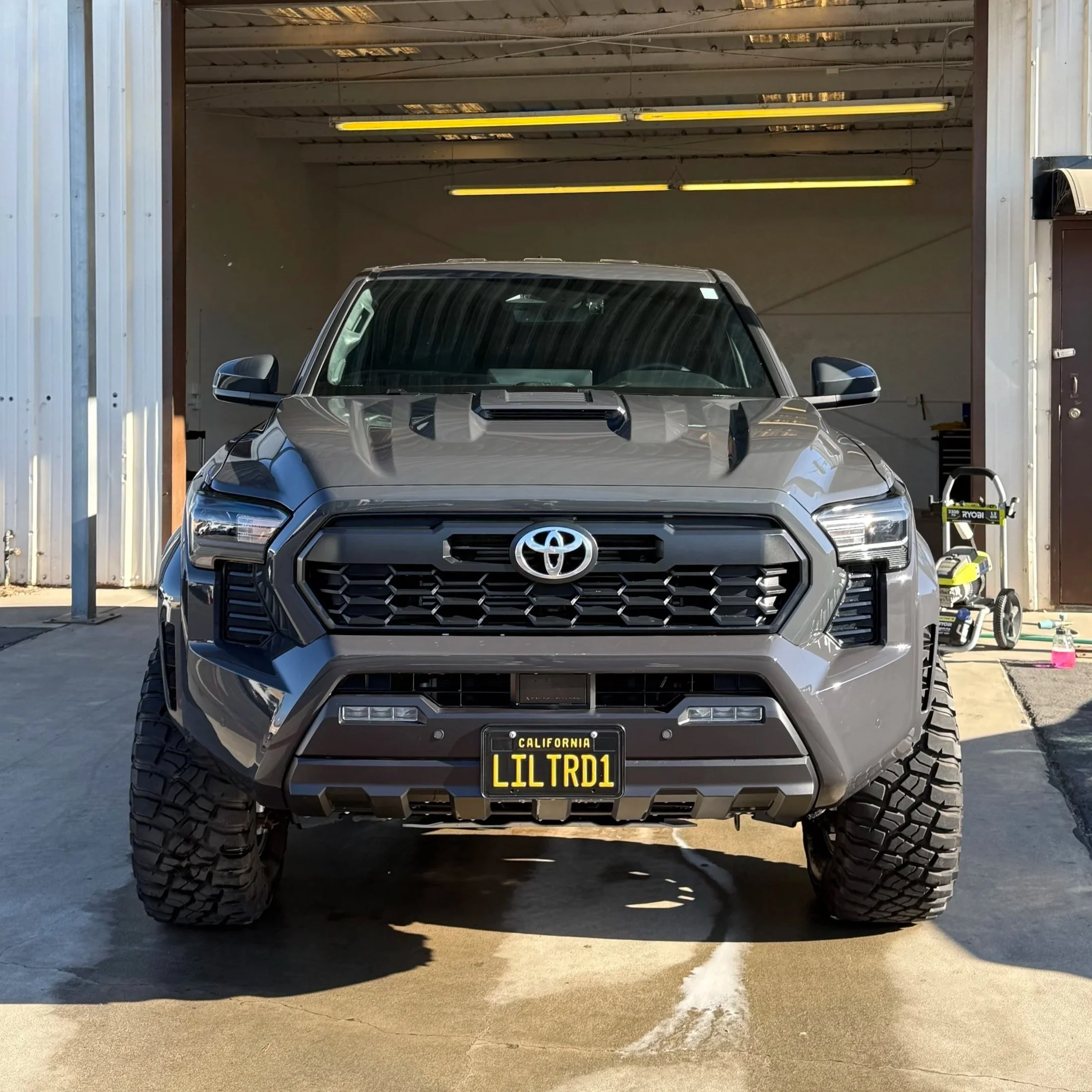 Front view of a gray Toyota pickup truck parked outside a garage, with off-road tires and wrapped in full body gloss clear paint protection film