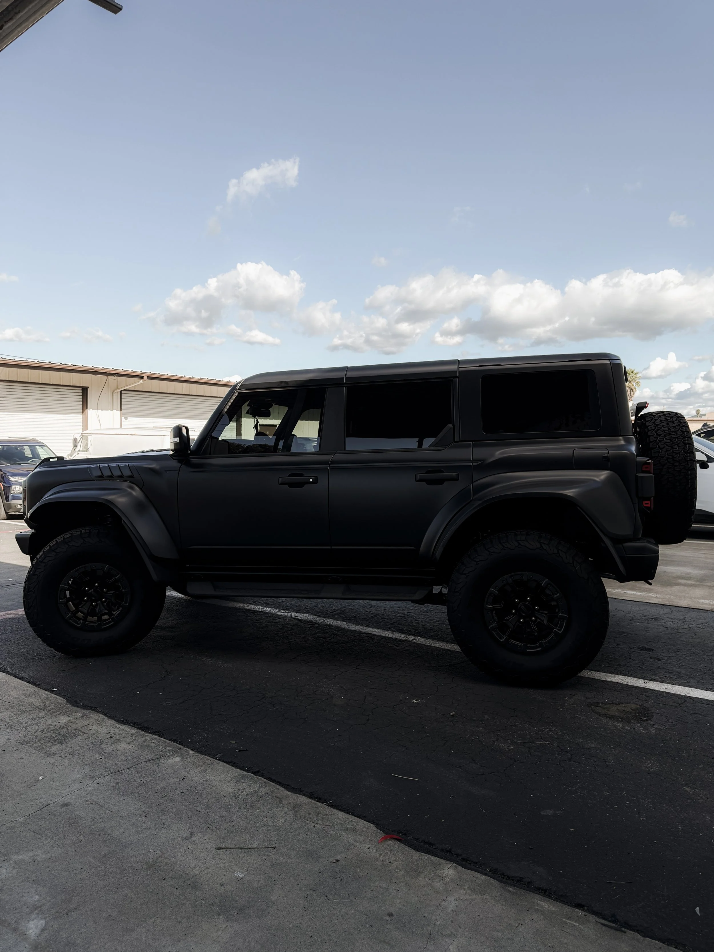 Black off-road SUV parked in a parking lot under a partly cloudy sky.