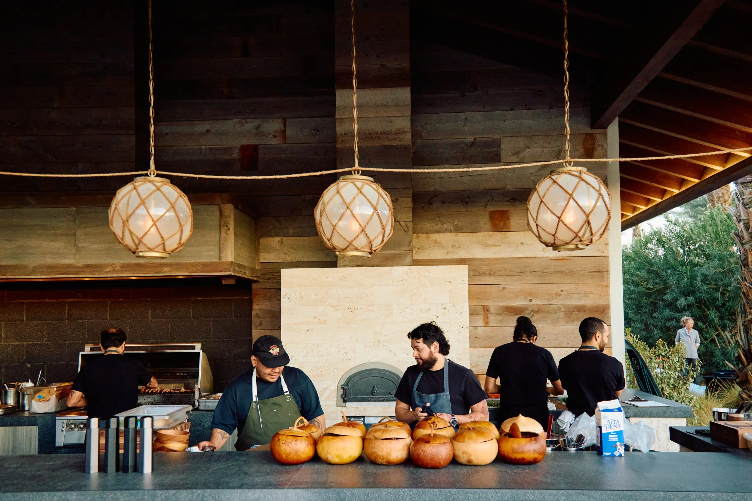 Four chefs working behind a counter at a restaurant, with pumpkins on the counter and warm lighting fixtures overhead.