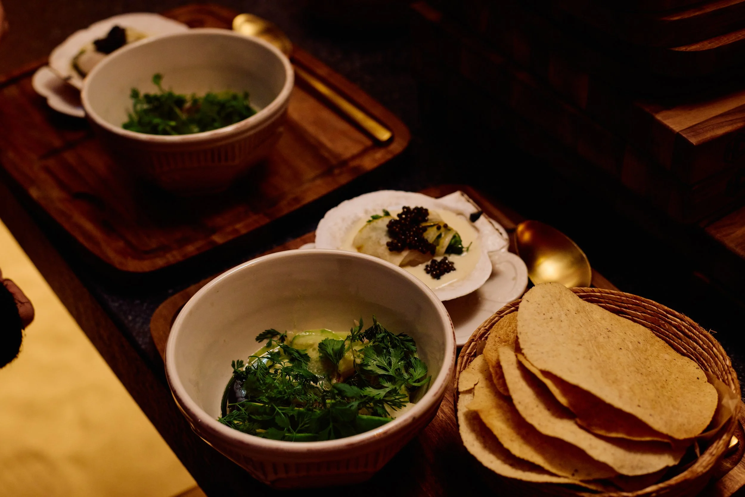 Wooden table with bowls of fresh herbs, slices of bread, and a dish with black caviar and a cream spread topped with caviar.