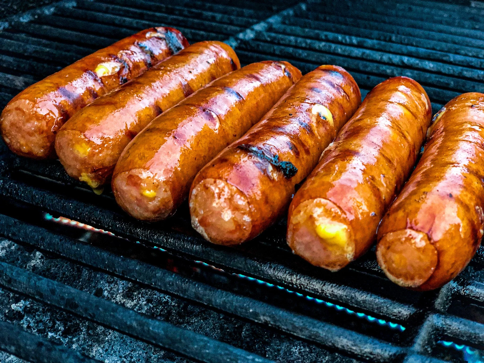 Six hot dogs on a grill with grill marks and glowing heat.