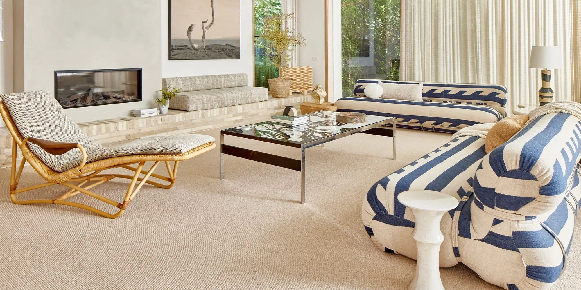 Living room with striped sofas, a modern coffee table, a woven lounge chair, a fireplace, large windows with curtains, and various decorative items.