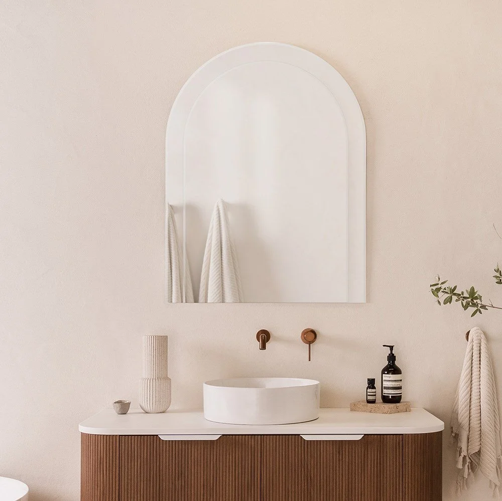Modern bathroom vanity with a round white vessel sink, wall-mounted copper faucet, large mirror, decorative vases, soap dispenser, and towels.