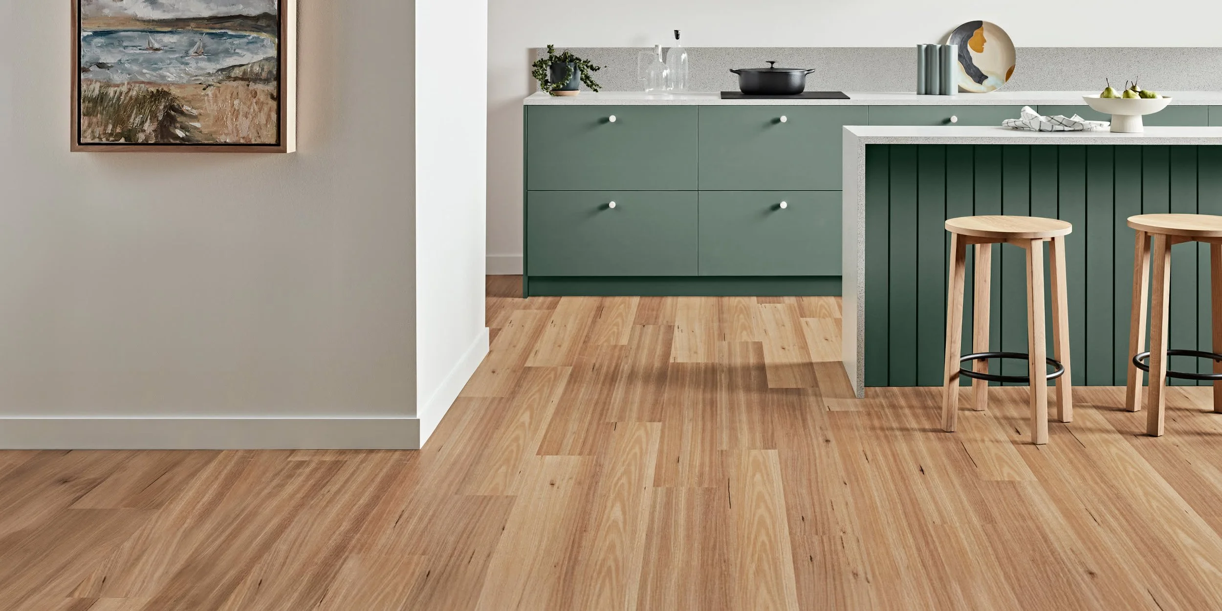 Modern kitchen with green cabinetry, a white countertop, and wooden bar stools on hardwood flooring.