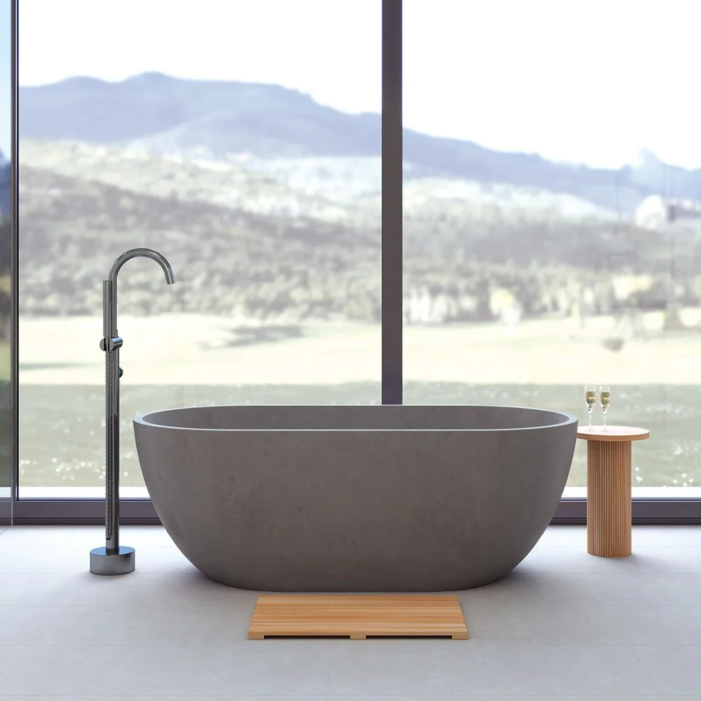 Modern bathroom with a large gray free-standing bathtub, a floor-mounted silver faucet, a small round wooden side table with two glasses of champagne, and a view of mountains through floor-to-ceiling windows.