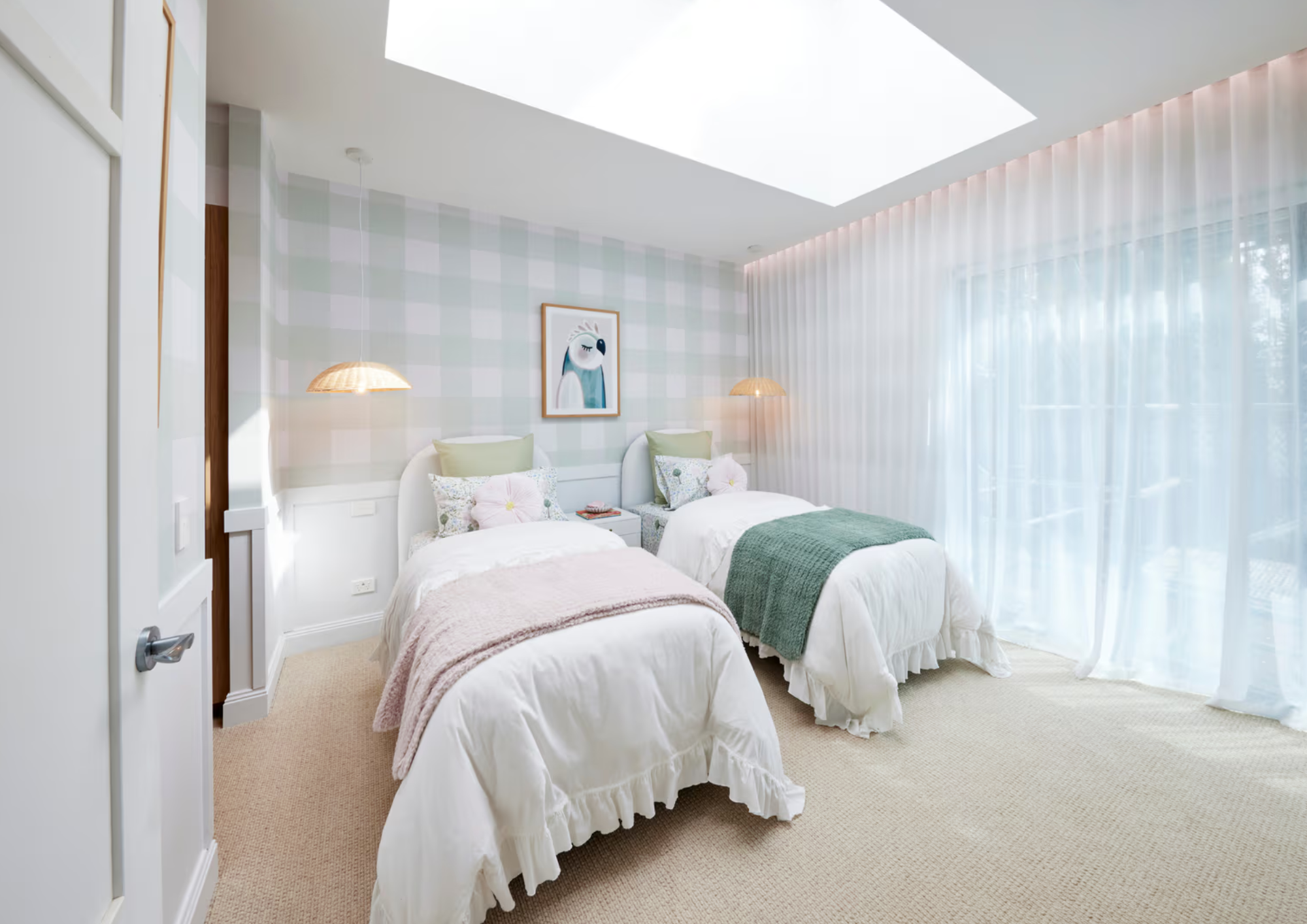 Bright bedroom with two twin beds, pastel pillows, wall art of a bird, and sheer curtains next to large window