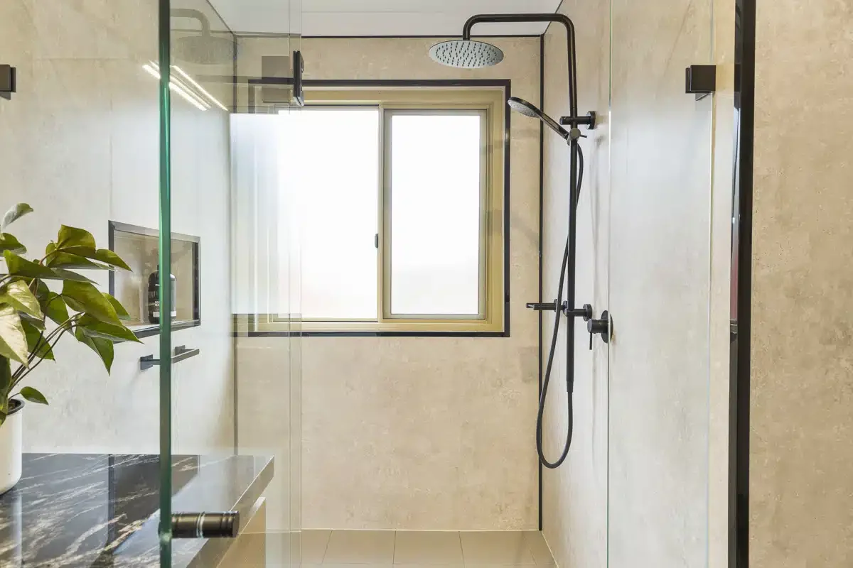 Modern shower with a rainfall showerhead, a handheld shower attachment, and a glass partition in a minimalistic bathroom.