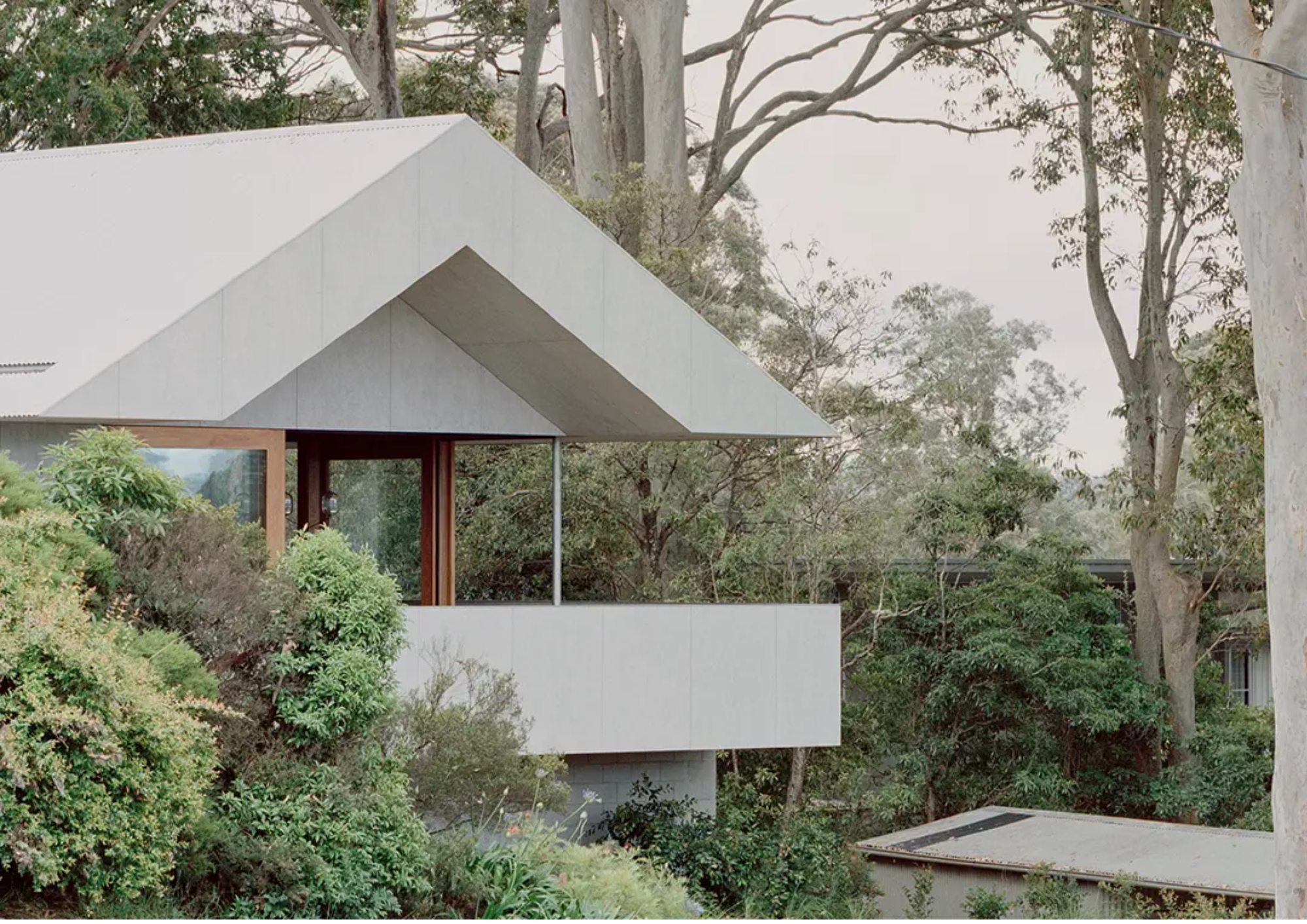 Modern house with white angular roof surrounded by green trees and bushes
