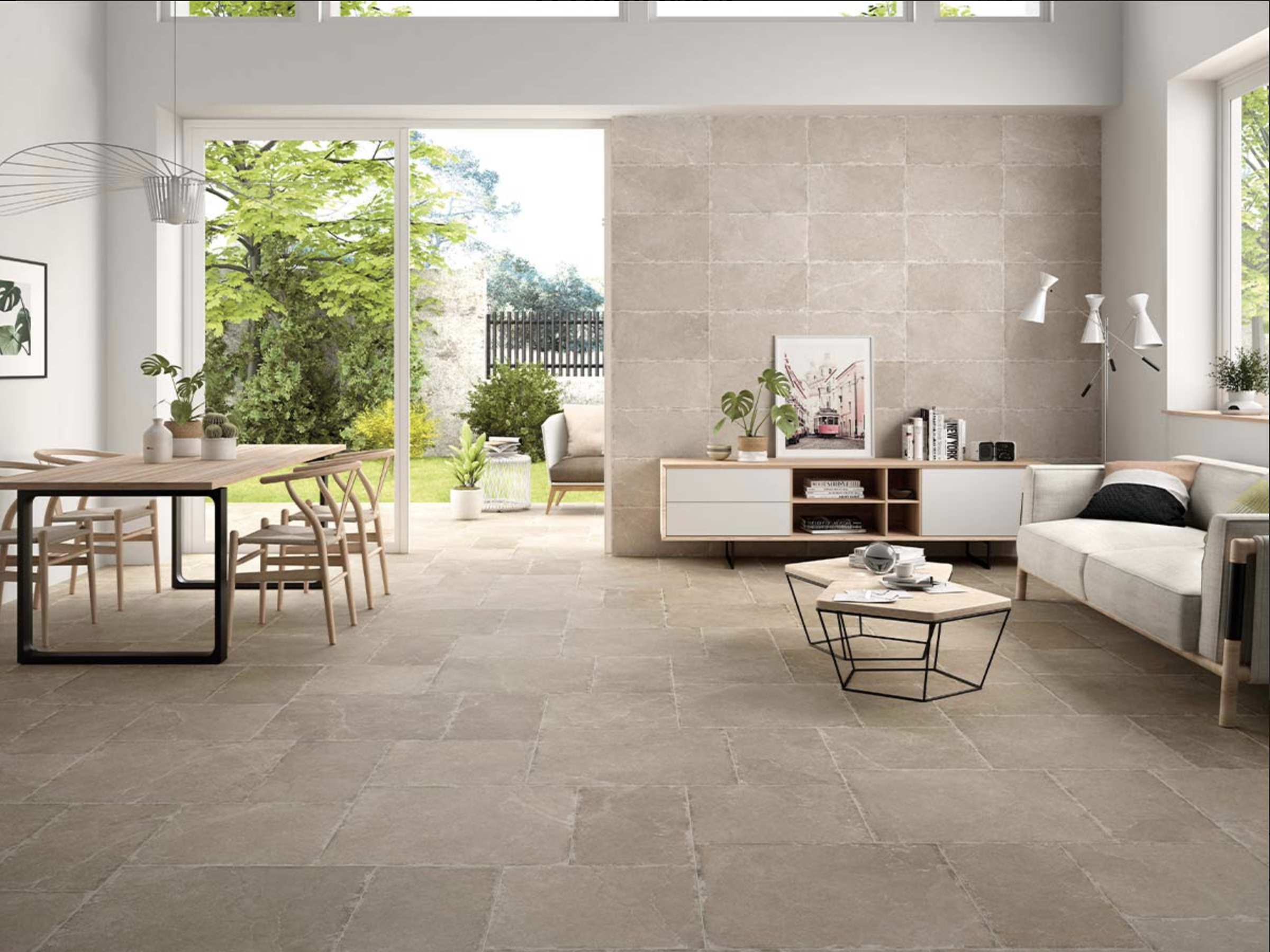 Living room with beige tiled floor, white walls, and large sliding glass doors leading to a garden patio with outdoor seating, trees, and greenery.