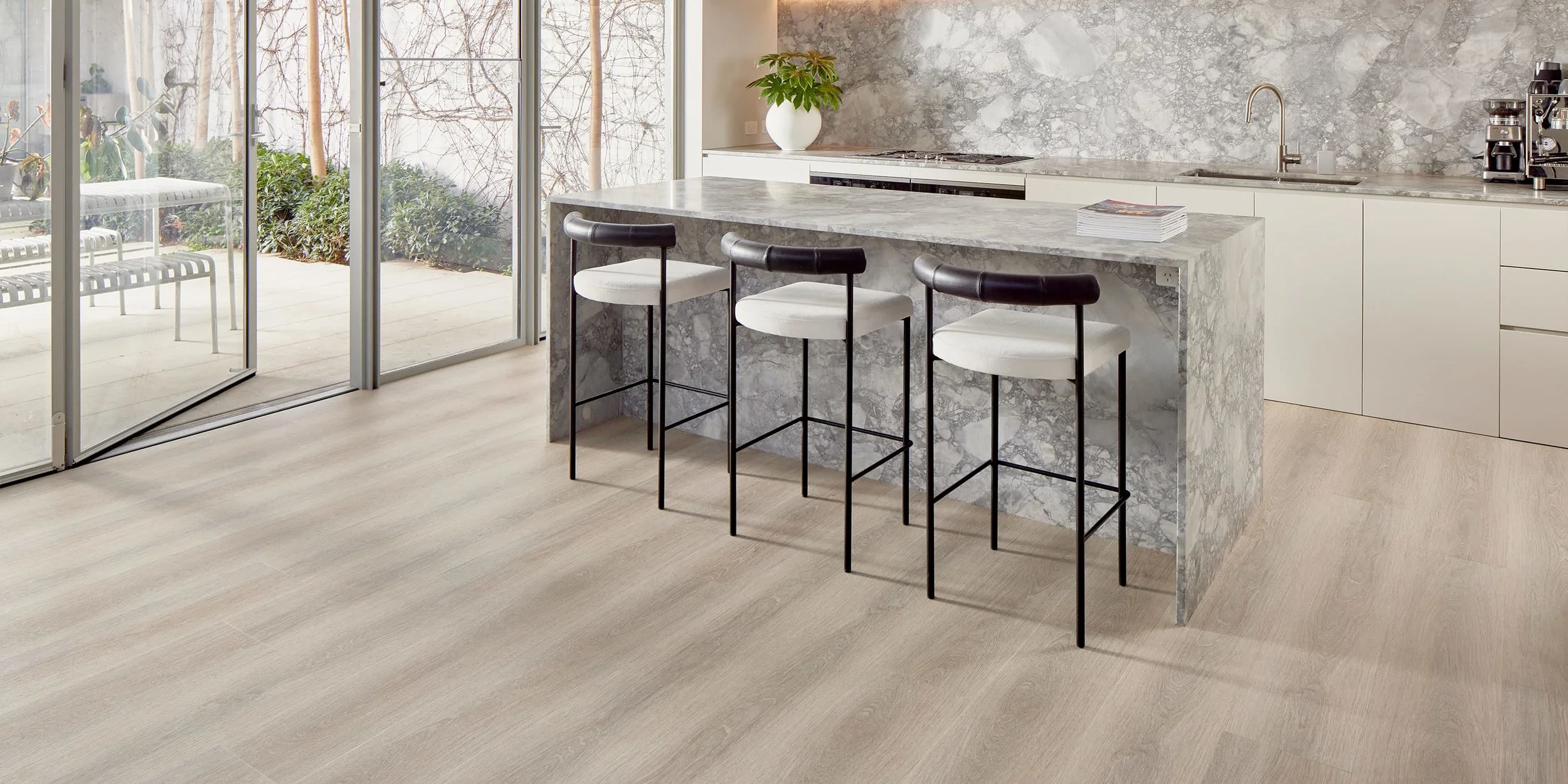 Modern kitchen with a marble island, three barstools, and floor-to-ceiling sliding glass doors leading to an outdoor patio.