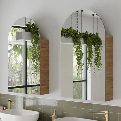 Two arched mirrors above a bathroom sink with greenery hanging from the ceiling.