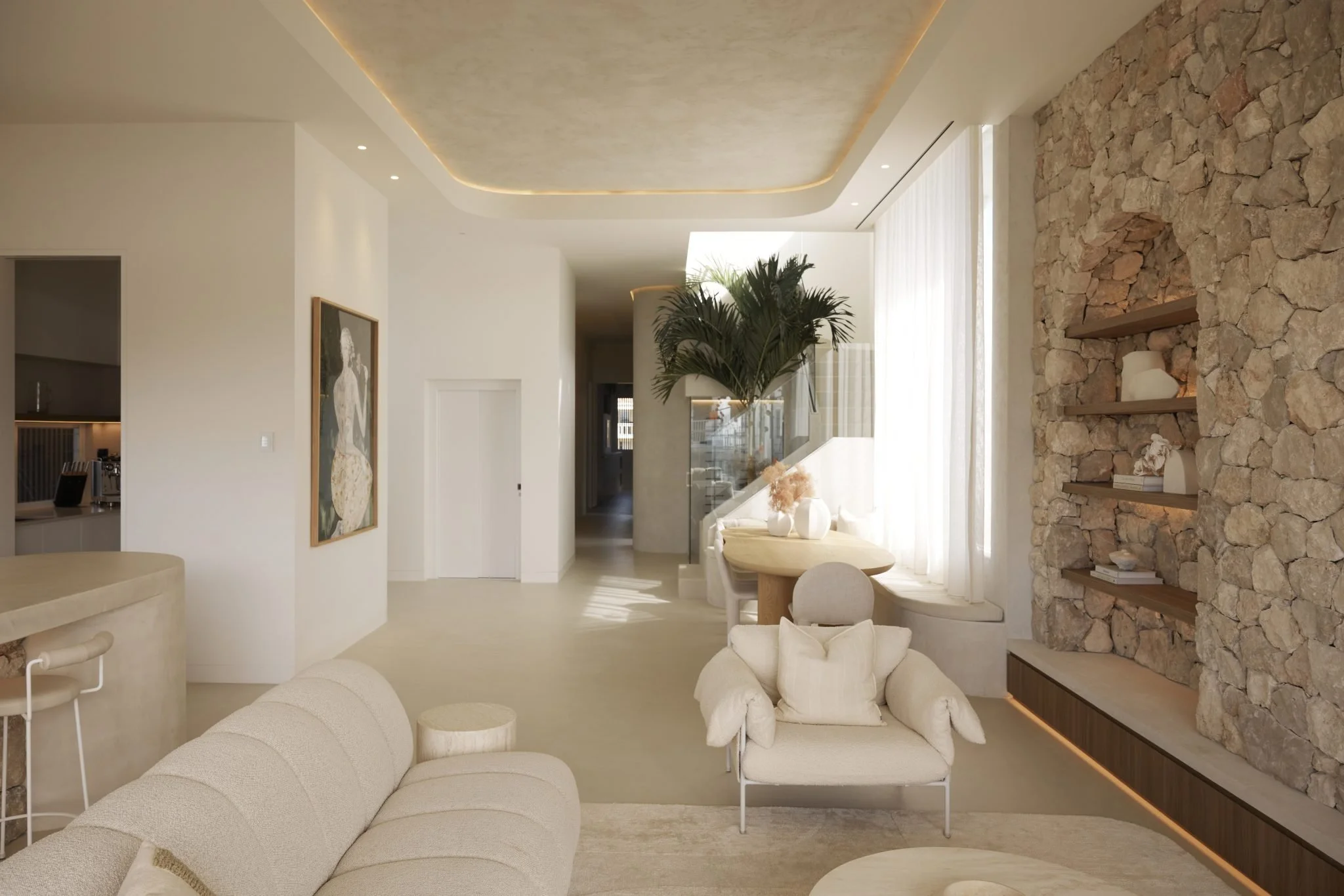 Modern living room with beige sofa, armchair with pillows, stone accent wall with built-in shelves, large plant near window with white curtains, and minimalistic decor.