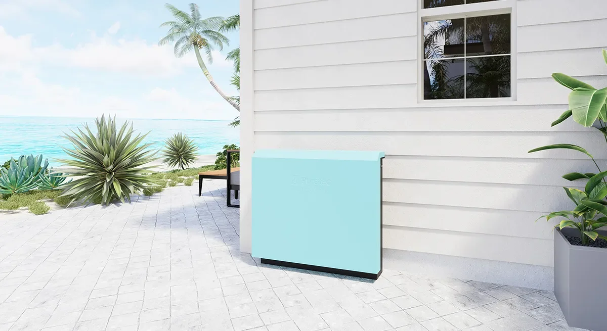 Exterior of a house with a view of the ocean, potted plants, a lounge chair, and an ice maker on a patio.